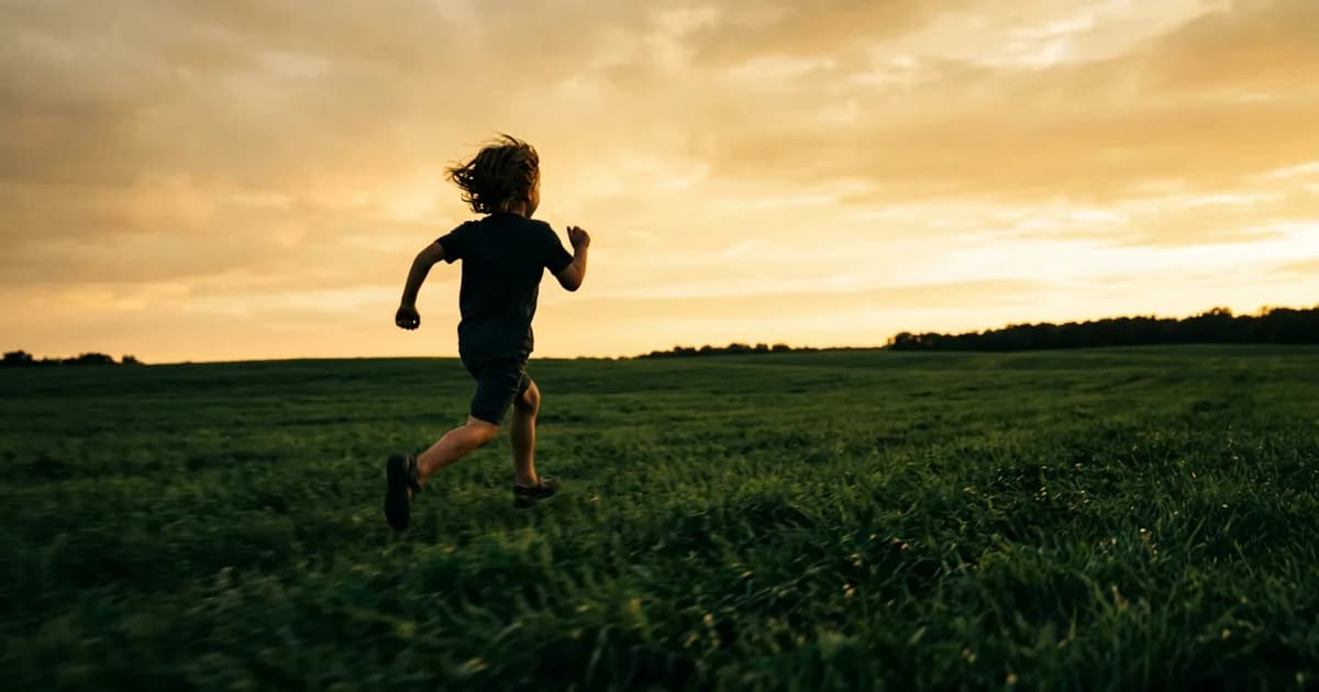 A child running through a sunlit open field, photographed from behind, arms wide, pure motion and joy